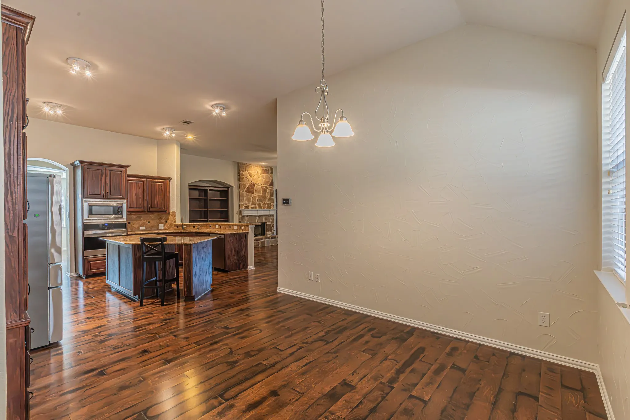 Vaulted ceilings, wood-finish flooring, recessed lighting, and a multi-light chandelier define this space, which includes a kitchen featuring built-in cabinetry and a stone-accented fireplace
