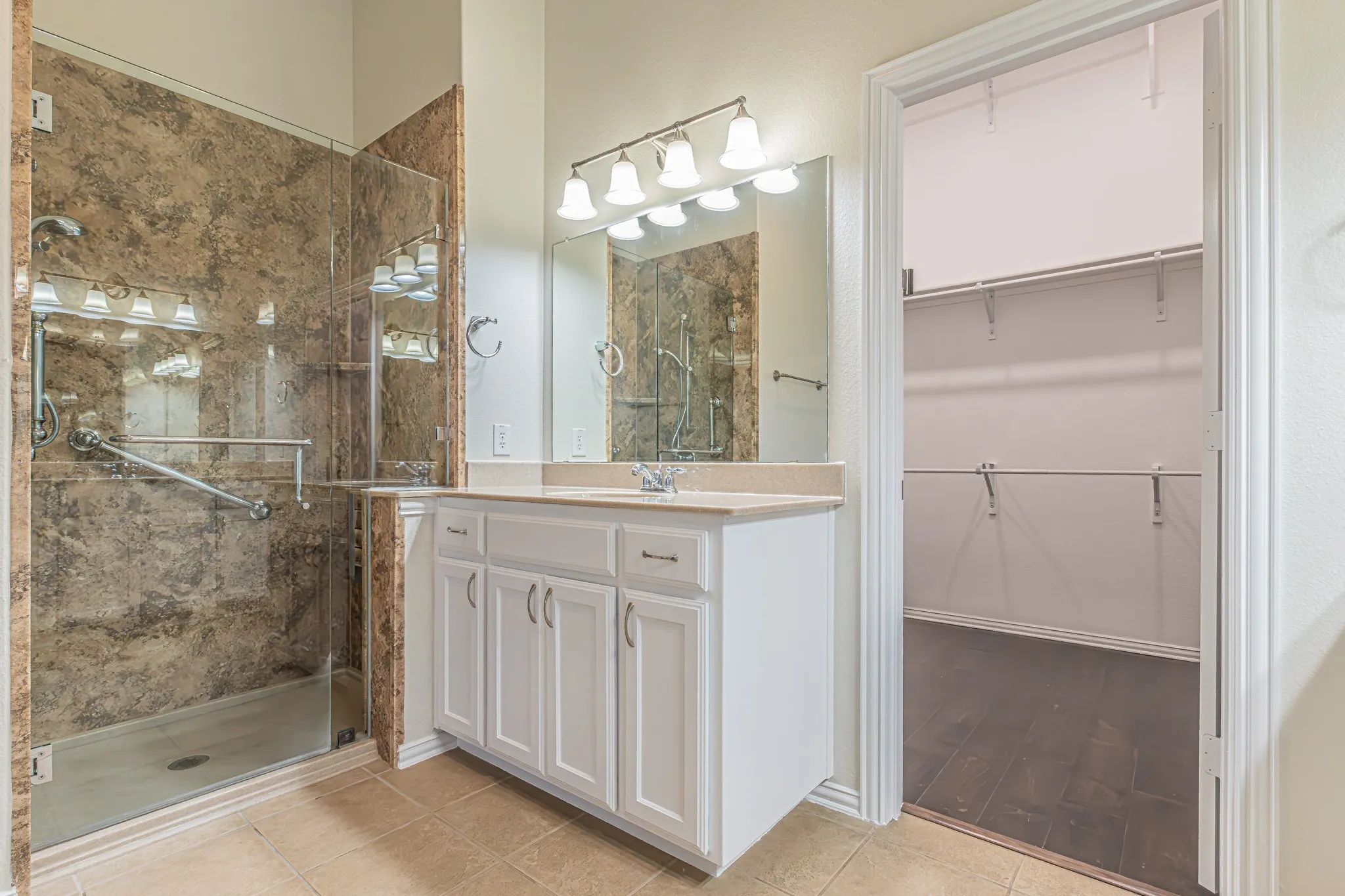Bathroom featuring a white vanity with a neutral countertop, glass-enclosed shower with tiled surround, and walk-in closet with wood-finish flooring