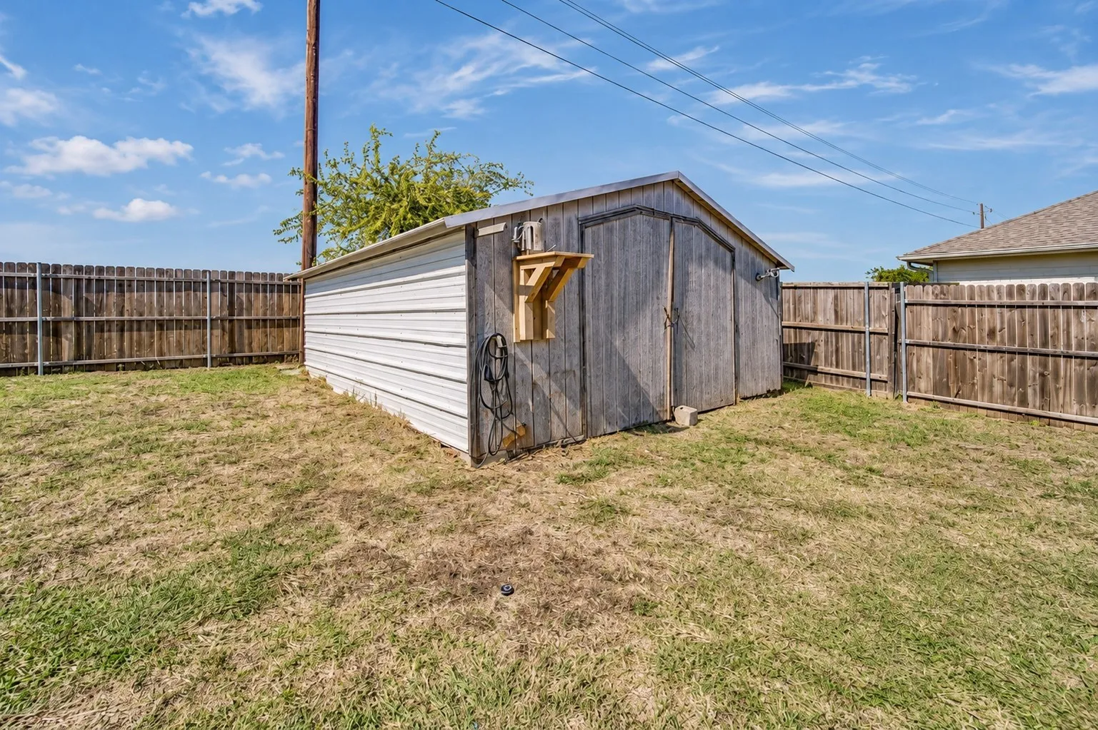 Exterior storage shed featuring corrugated metal siding, double swinging doors, and a wood-slatted exterior wall, situated within a fenced backyard