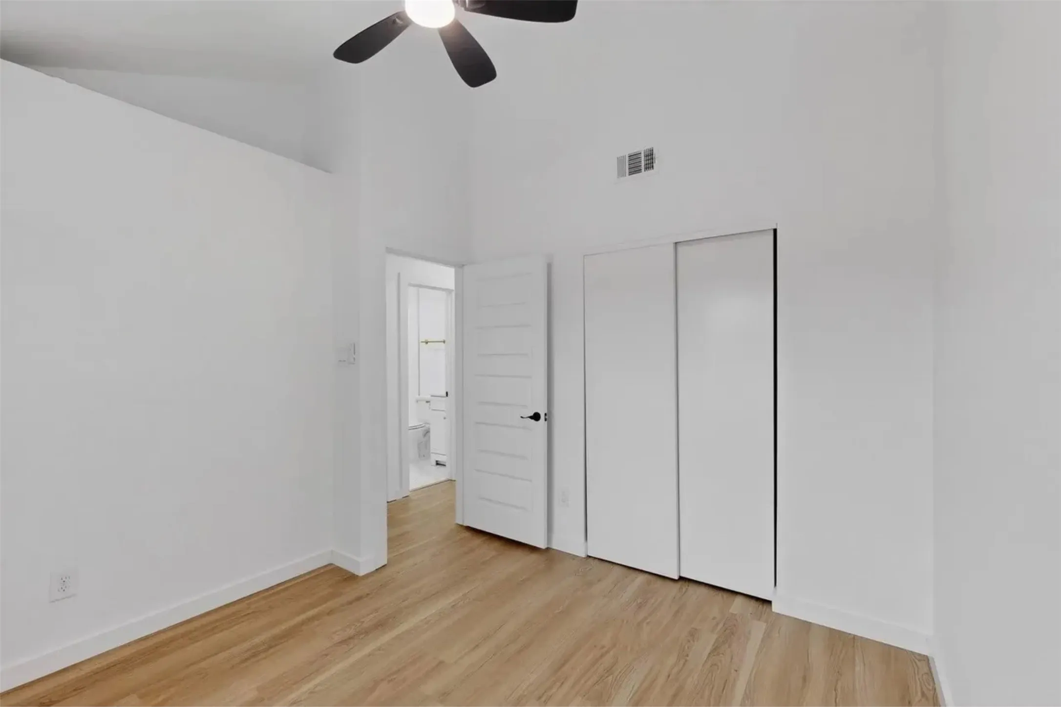 Vaulted ceilings, wood-finish flooring, sliding closet doors, and an attached ceiling fan with integrated lighting