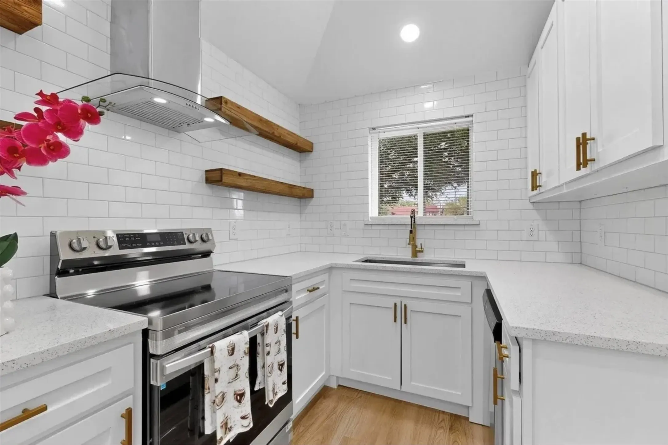 Kitchen featuring white shaker-style cabinetry, quartz countertops, white subway tile backsplash, stainless steel range with integrated exhaust hood, and wood-finish open shelving