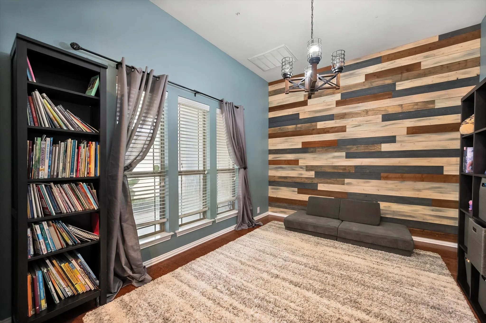 Additional living room has decorative lighting and wood accent wall.