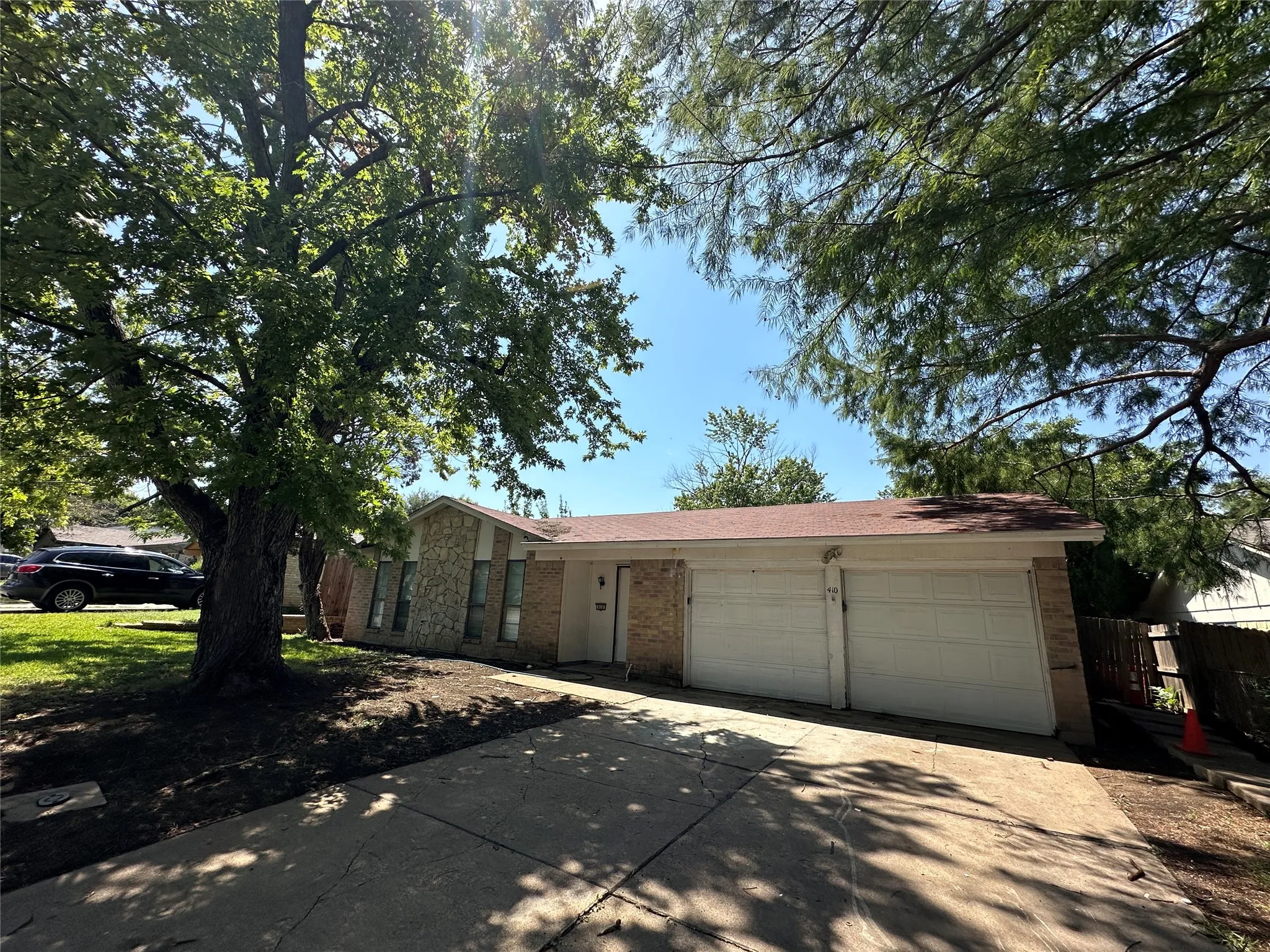 Single-story brick and stone facade with an attached two-car garage, concrete driveway, and mature canopy trees