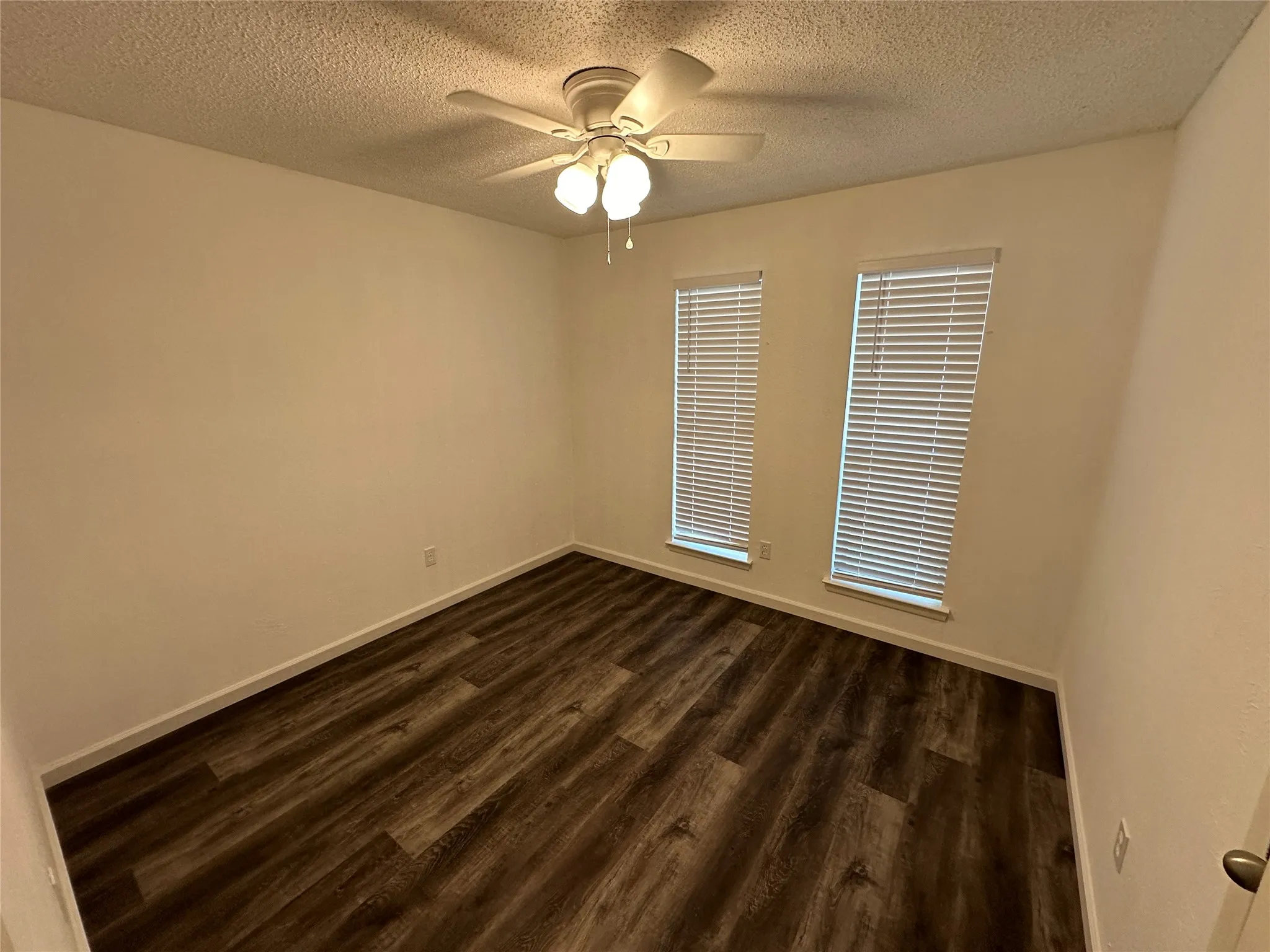 Wood-finish flooring, dual windows with installed blinds, and a central ceiling fan with integrated lighting