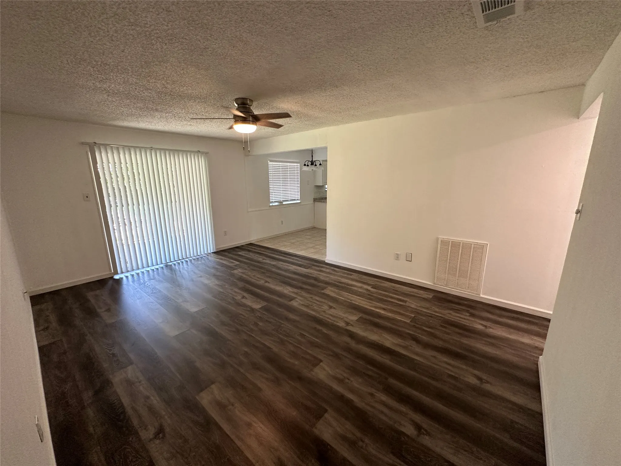 Wood-finish flooring, vertical slat blinds, and a ceiling fan with integrated lighting