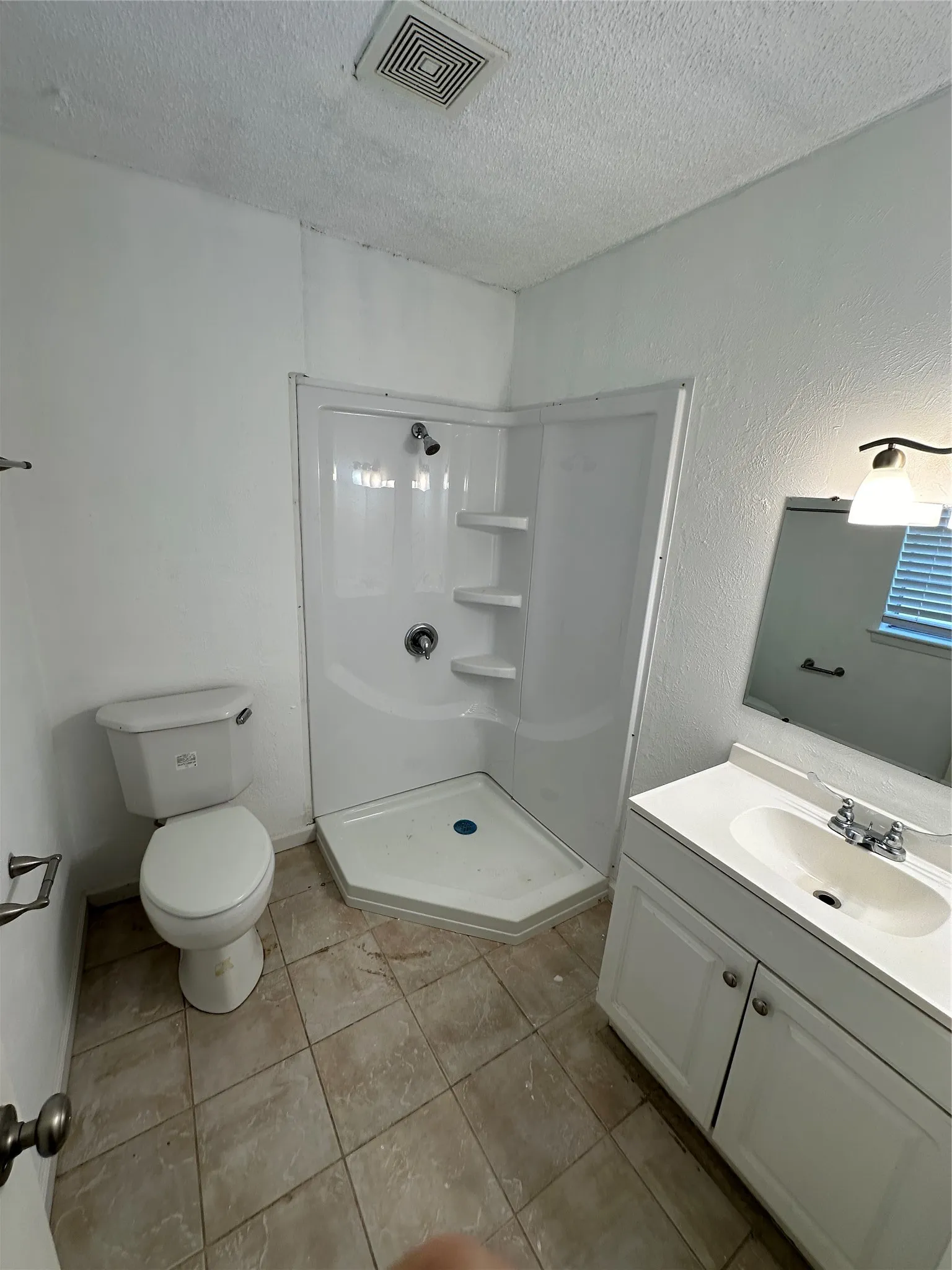 Bathroom featuring a corner shower unit with built-in shelving, white vanity cabinet with a drop-in sink, wall-mounted mirror, and tile flooring