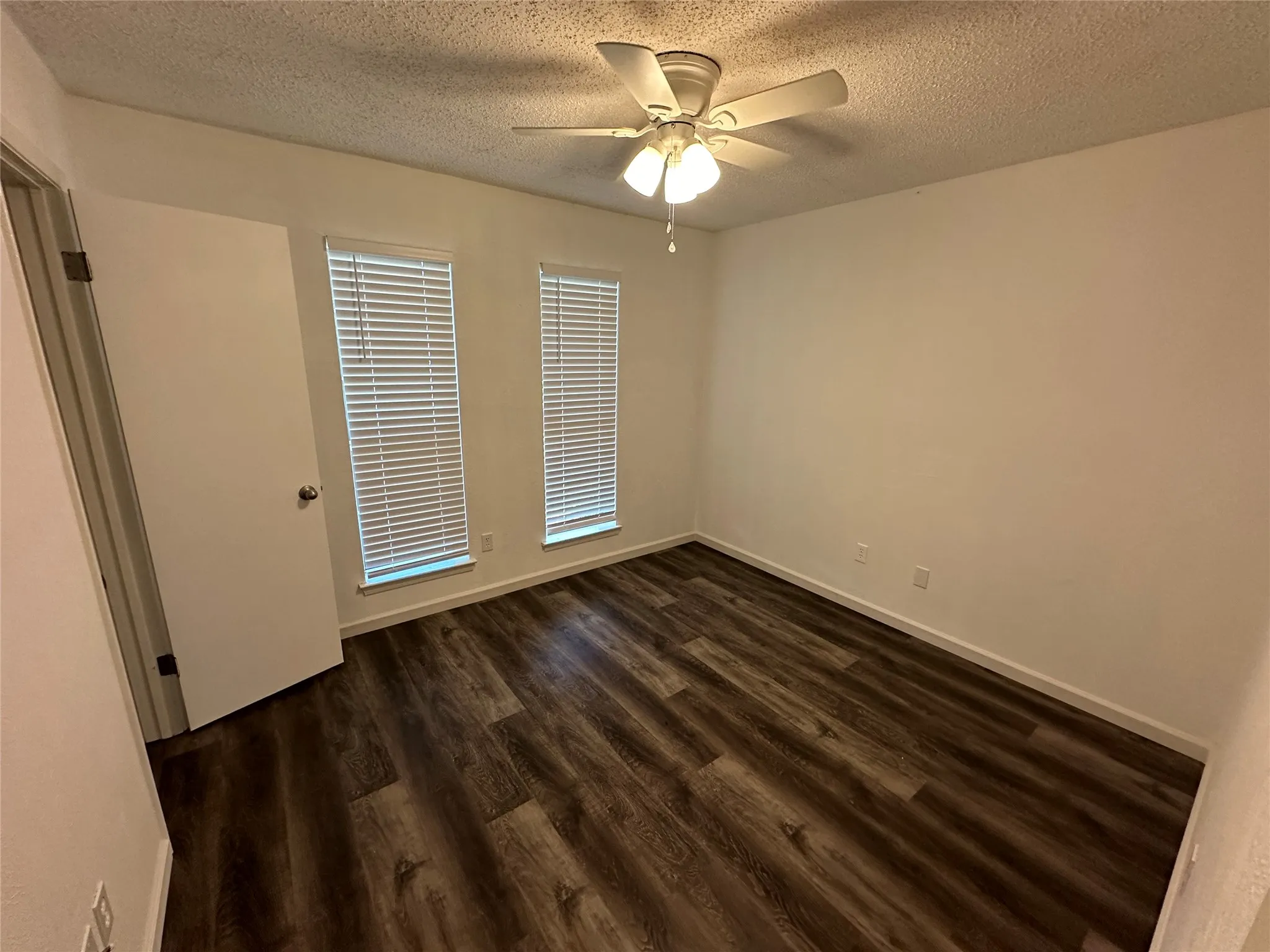 Room featuring wood-finish flooring, dual windows with horizontal blinds, and a central ceiling fan with integrated lighting