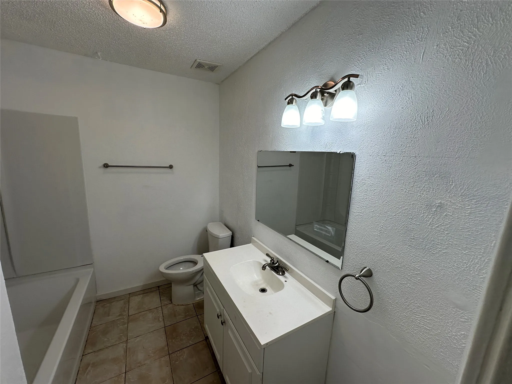 Bathroom featuring a vanity with an integrated basin, a three-light fixture, a wall-mounted mirror, ceramic tile flooring, and a tub-shower combination