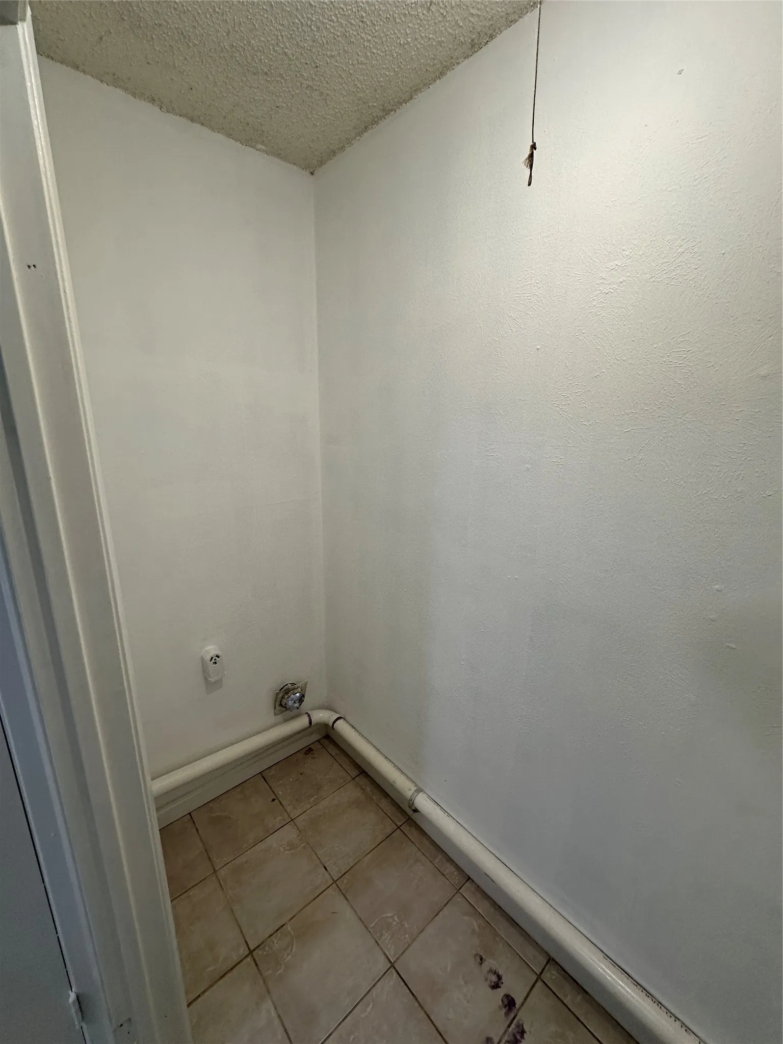Dedicated utility space featuring neutral ceramic floor tiling, white walls, and built-in plumbing infrastructure