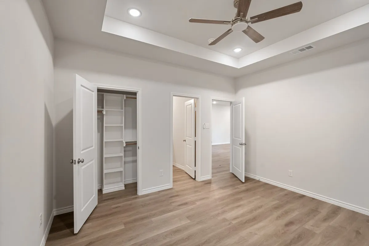 Tray ceiling with recessed lighting, wood-finish flooring, ceiling fan, and built-in closet shelving