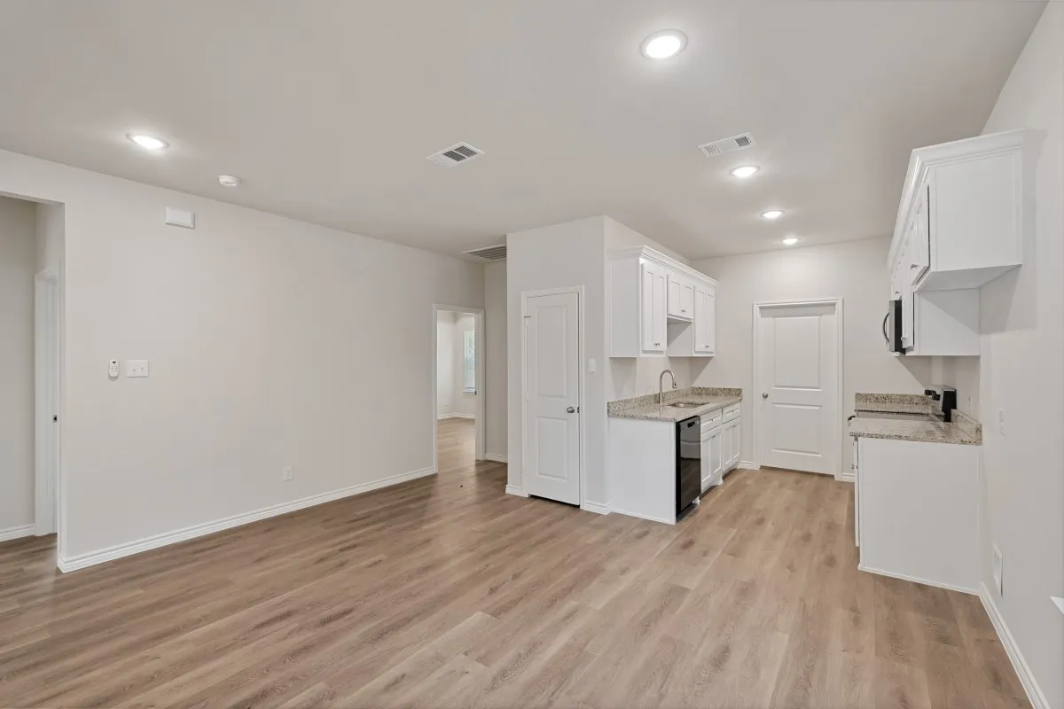 Open interior space featuring wood-finish flooring, recessed lighting, white cabinetry, neutral stone-finish countertops, and a stainless steel sink