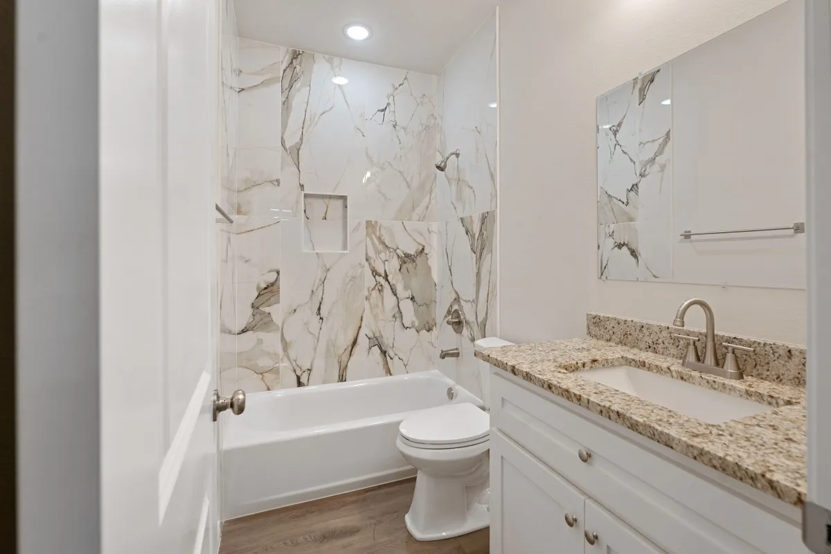 Bathroom featuring a tub-shower combination with floor-to-ceiling stone-pattern tile surround, built-in wall niche, vanity with stone-surface countertop and integrated sink, and wood-finish flooring