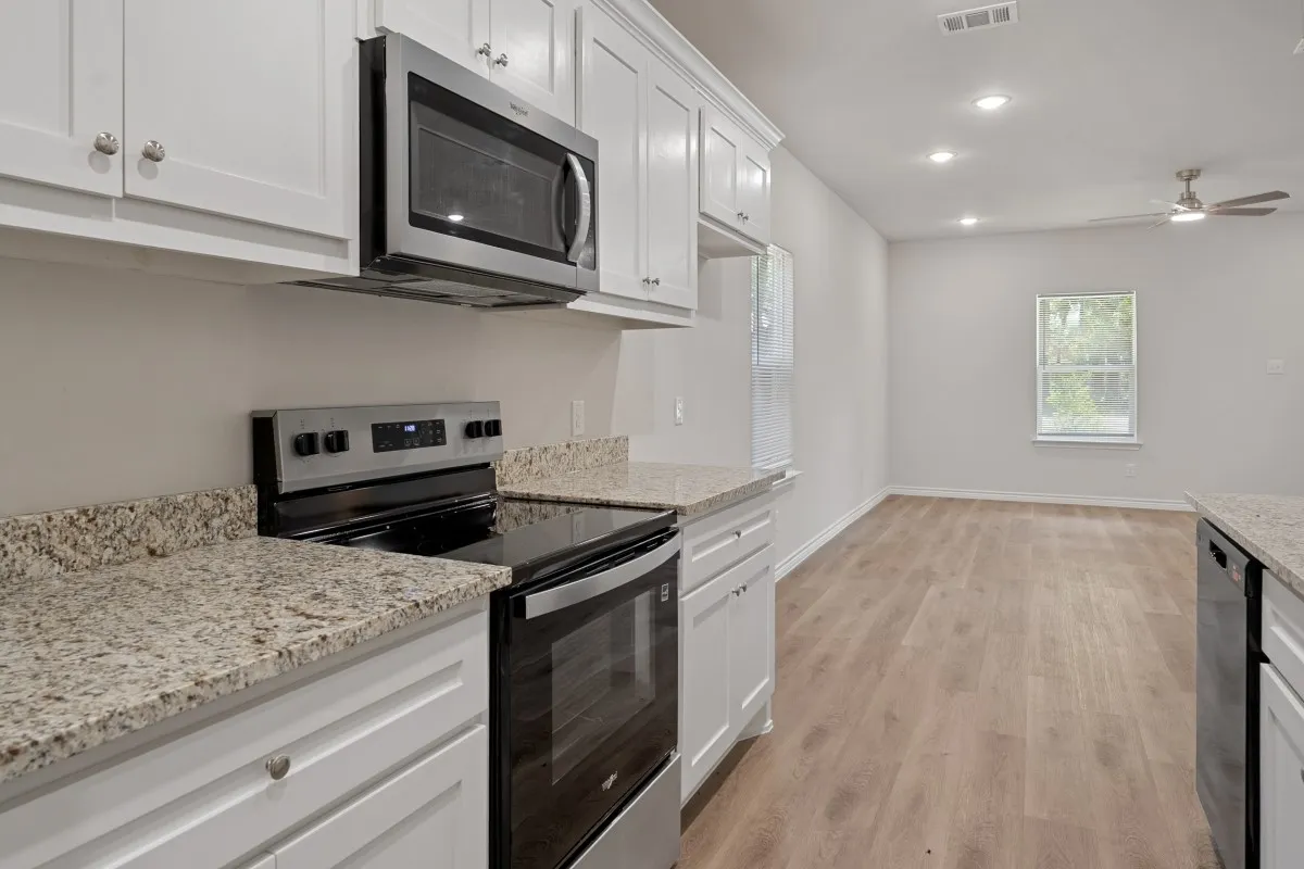 Kitchen featuring white shaker-style cabinetry, stone-finish countertops, stainless steel appliances, and wood-finish flooring
