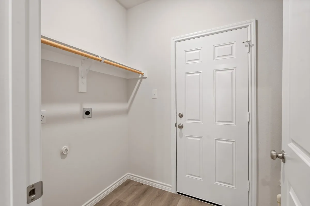 Utility room featuring wood-finish flooring, a six-panel door, and a built-in wall-mounted garment rod
