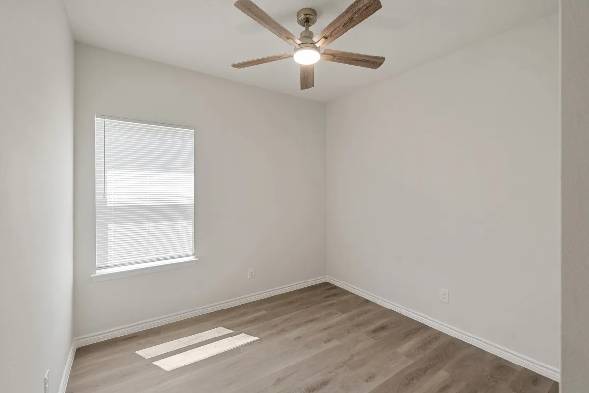 Neutral-toned interior space featuring wood-finish flooring, a ceiling fan with integrated lighting, and a single-hung window with installed blinds
