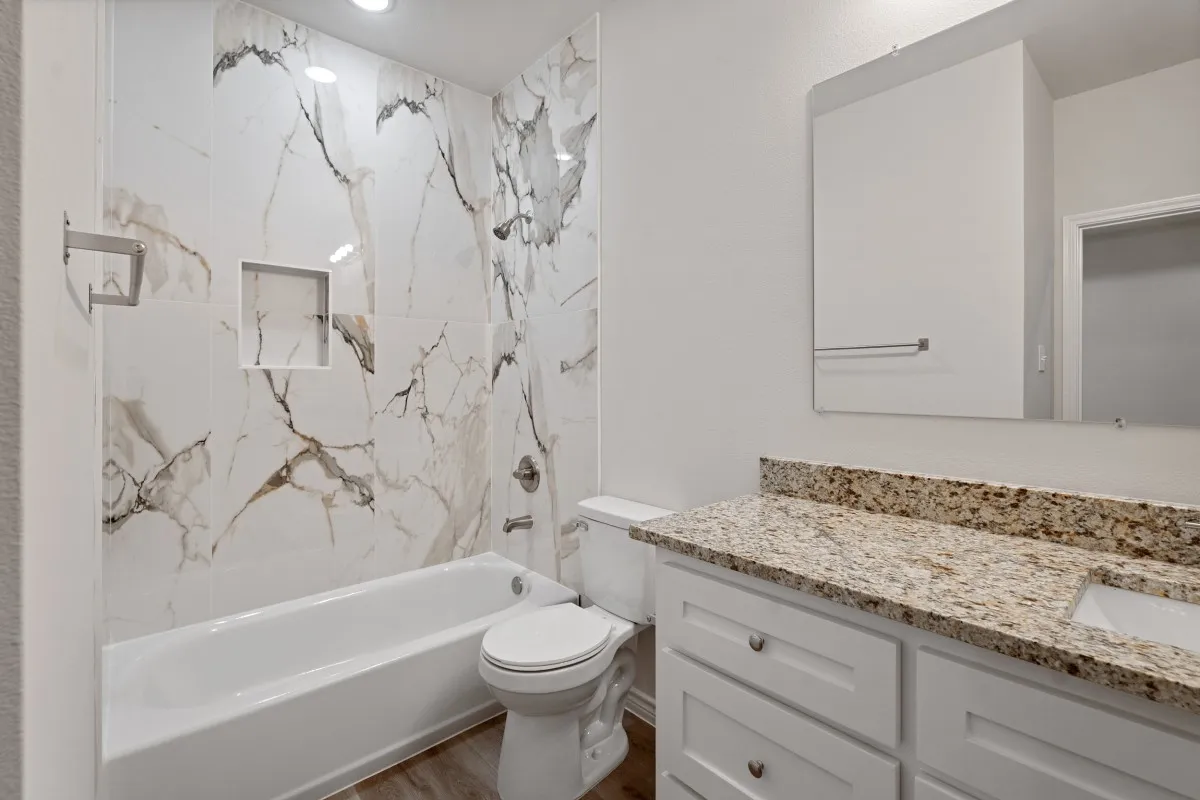Bathroom featuring full-height stone-patterned wall tile, built-in shower niche, vanity with stone-finished countertop, undermount sink, and white cabinetry
