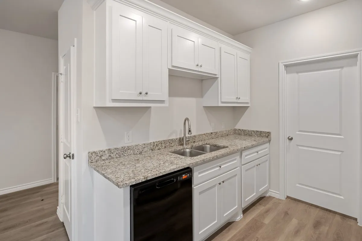 White shaker-style cabinetry, stone-finish countertops, stainless steel dual-basin sink with arched faucet, black built-in dishwasher, and wood-finish flooring