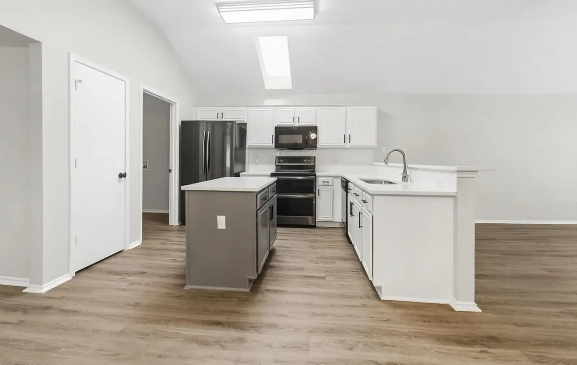 Kitchen featuring a center island, vaulted ceiling with a skylight, white cabinetry, light-toned countertops, and wood-finish flooring