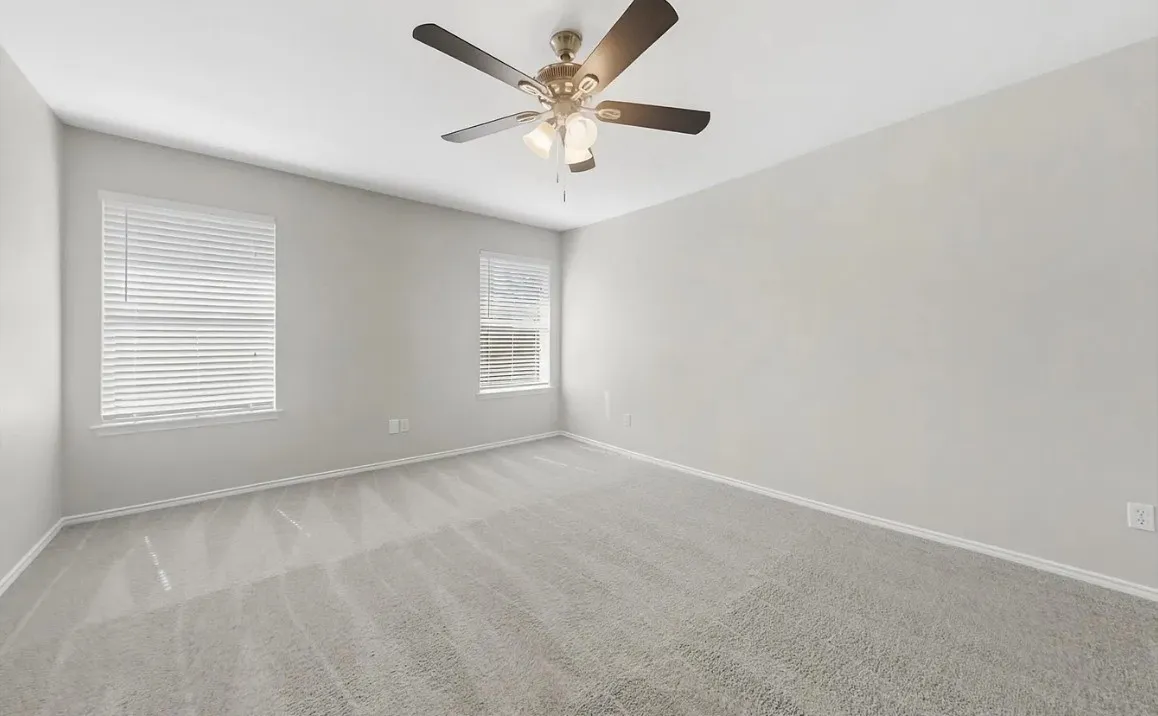 Neutral-toned interior space featuring wall-to-wall carpeting, dual windows with horizontal blinds, and a multi-light ceiling fan