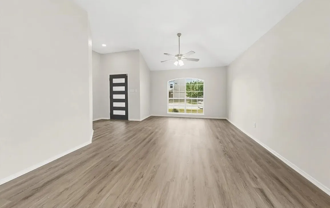 Open-concept living space featuring vaulted ceilings, wood-finish flooring, a multi-pane arched window, and a modern entry door with horizontal glass panels