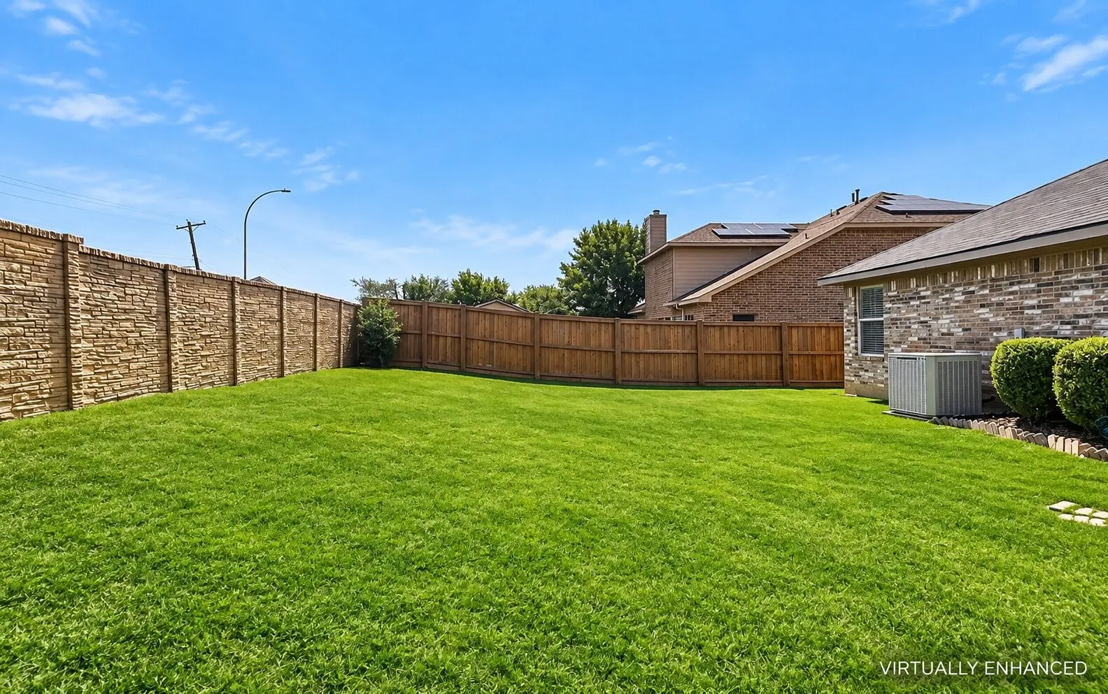 Spacious backyard featuring a manicured lawn, stone-textured privacy wall, and wood-panel fencing