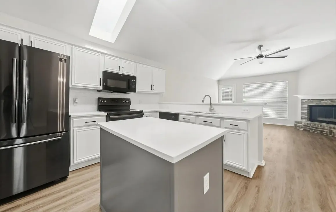 Kitchen featuring a central island with a solid surface countertop, white shaker-style cabinetry, stainless steel appliances, a vaulted ceiling with a skylight, and wood-finish flooring