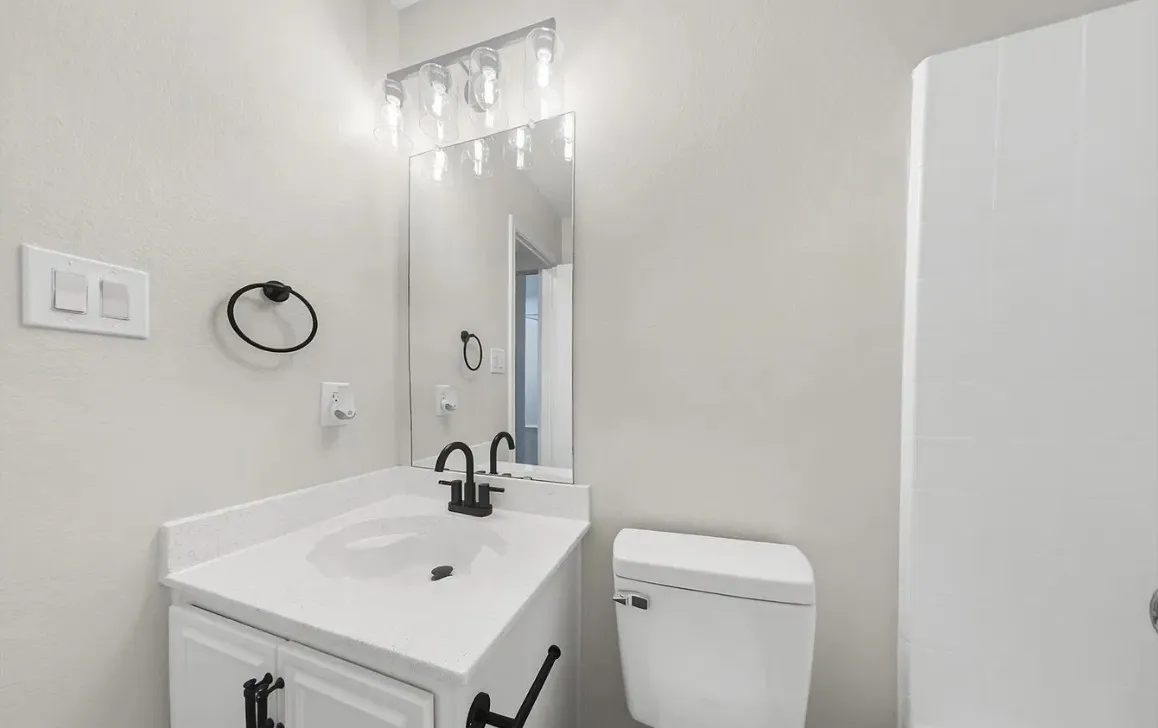 Bathroom featuring a vanity with a white countertop, matte black faucet, wall-mounted light fixture, mirror, and a circular towel ring
