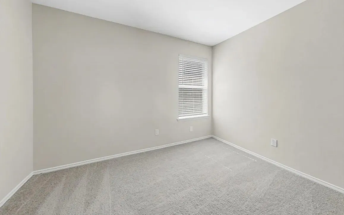 Neutral-toned interior room featuring wall-to-wall carpeting and a single window with installed horizontal blinds