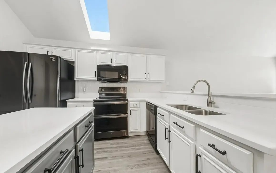 Kitchen featuring white cabinetry, solid-surface countertops, black appliances, wood-finish flooring, and a skylight