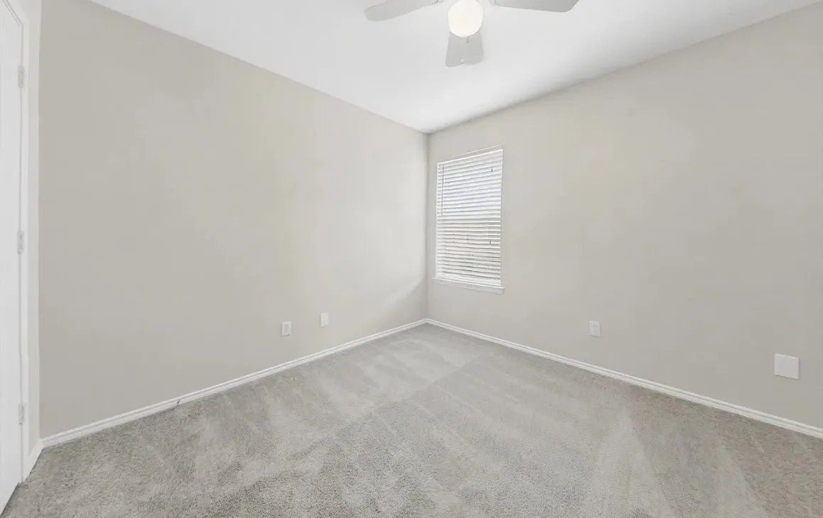 Neutral interior space featuring high-pile carpeting, neutral wall paint, a ceiling fan with integrated lighting, and a single-pane window with horizontal blinds