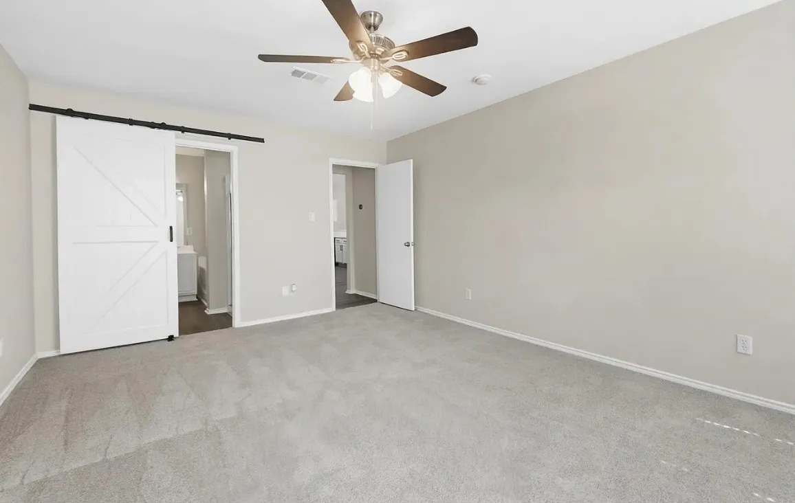 Interior space featuring neutral wall tones, wall-to-wall carpeting, a ceiling fan with integrated lighting, and a white sliding barn-style door on a black metal track