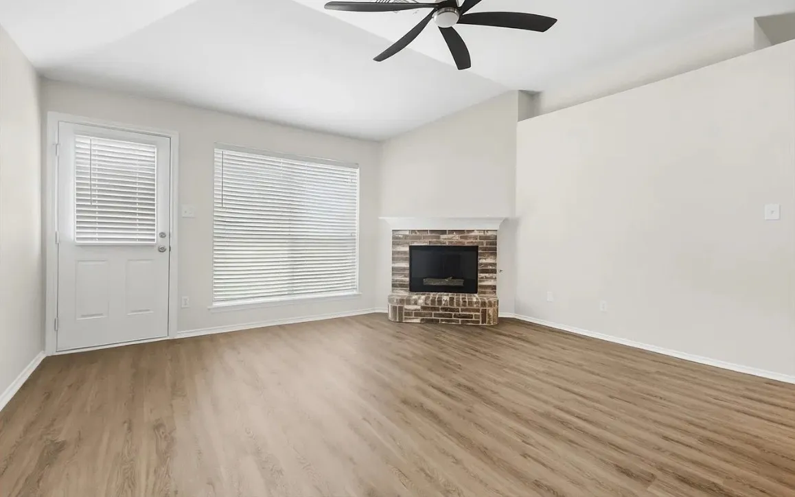 Vaulted ceiling with a matte black ceiling fan, wood-finish flooring, and a fireplace with a brick surround and mantel