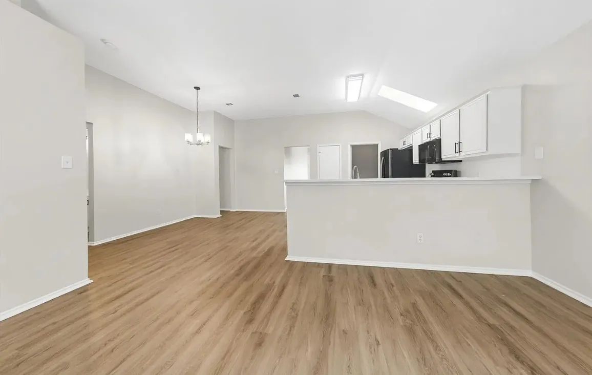 Open-concept space featuring wood-finish flooring, vaulted ceiling with a skylight, kitchen island with a breakfast bar, white cabinetry, and a tiered hanging light fixture