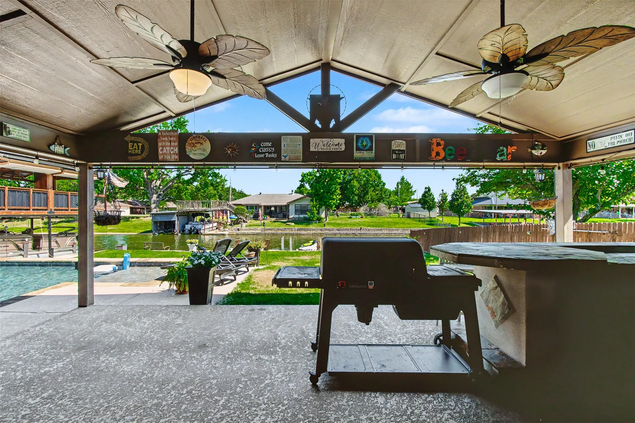 Covered outdoor patio featuring a vaulted ceiling with integrated ceiling fans, a built-in outdoor bar, and concrete flooring