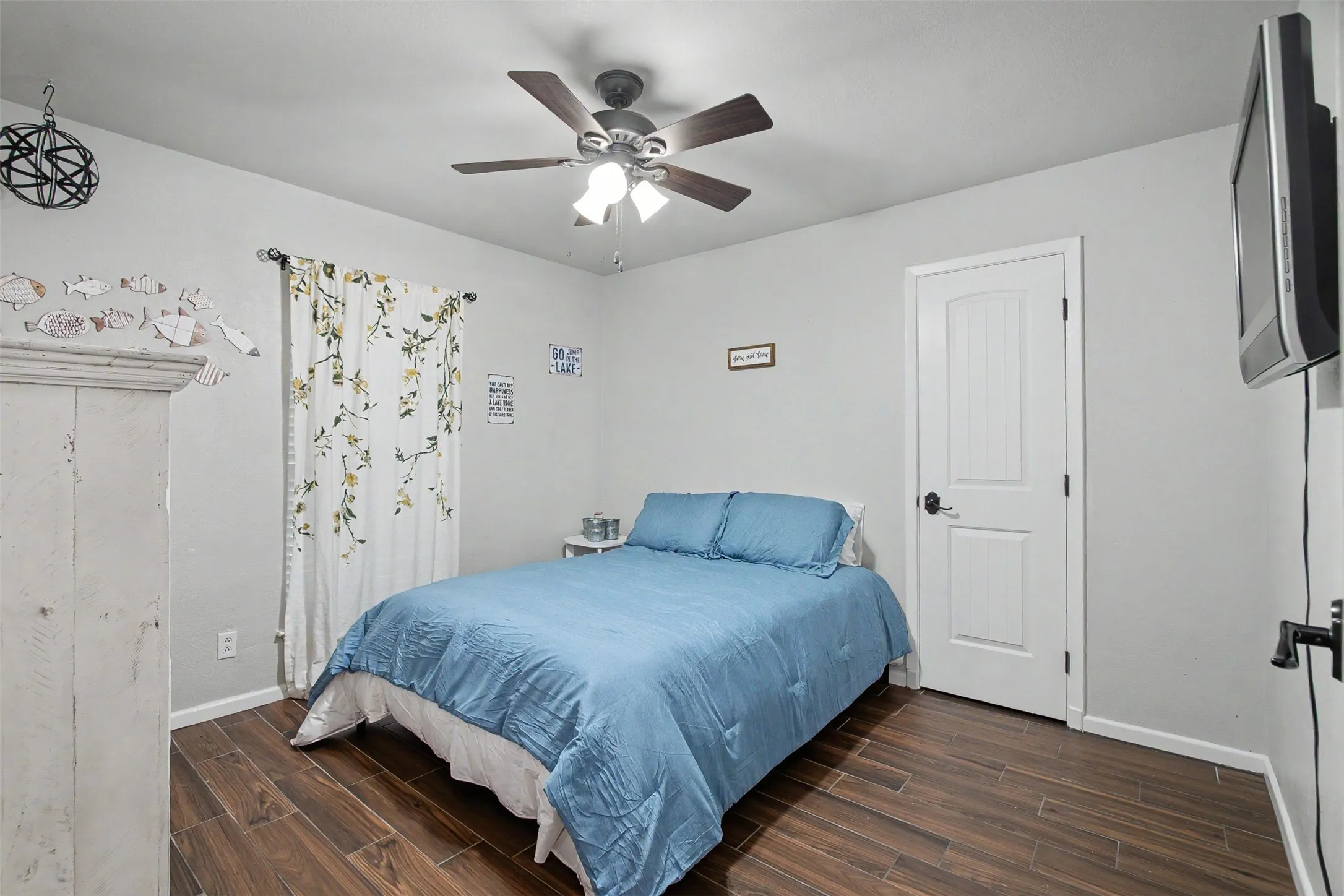 Interior space featuring wood-finish flooring, a multi-blade ceiling fan with integrated lighting, and a solid-core interior door with a matte black lever handle