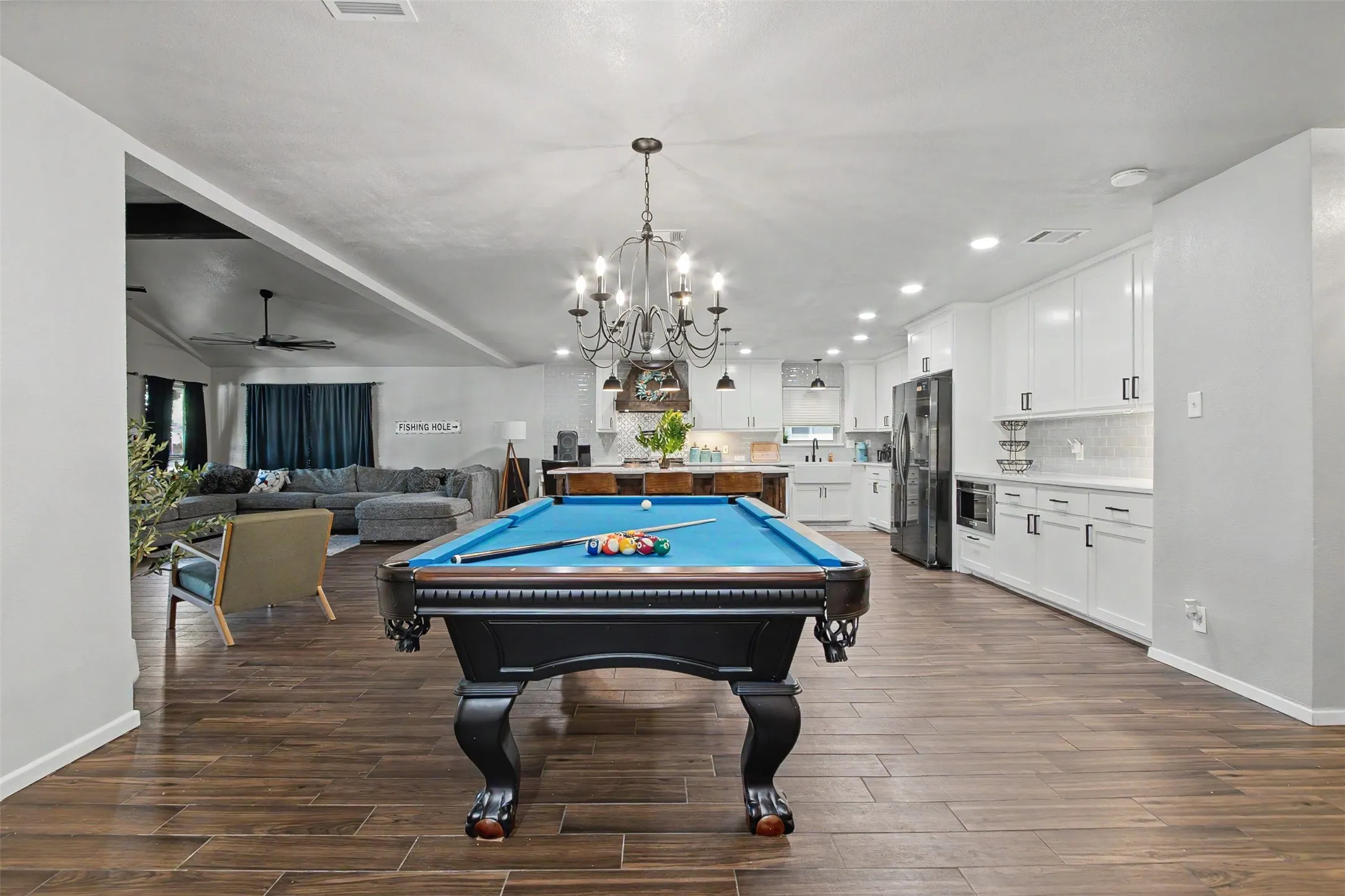 Open-concept interior featuring wood-finish flooring, a multi-arm iron chandelier, recessed lighting, and kitchen cabinetry with integrated appliances