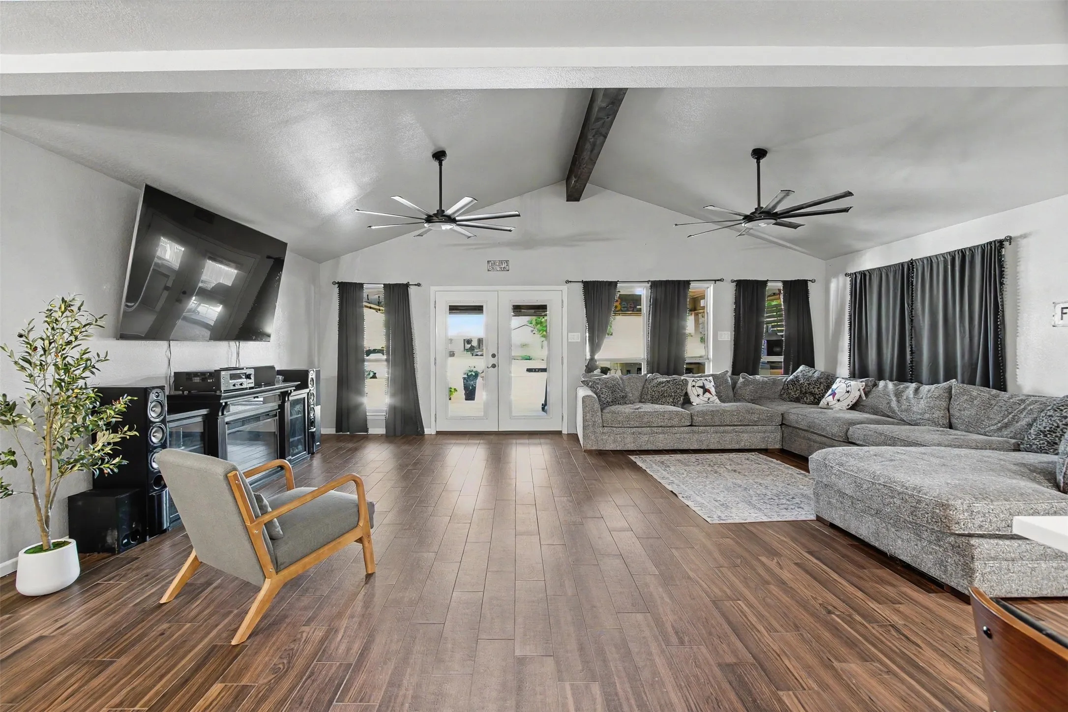 Vaulted ceilings with exposed decorative beam, wood-finish flooring, dual multi-blade ceiling fans, and glass-paneled double doors