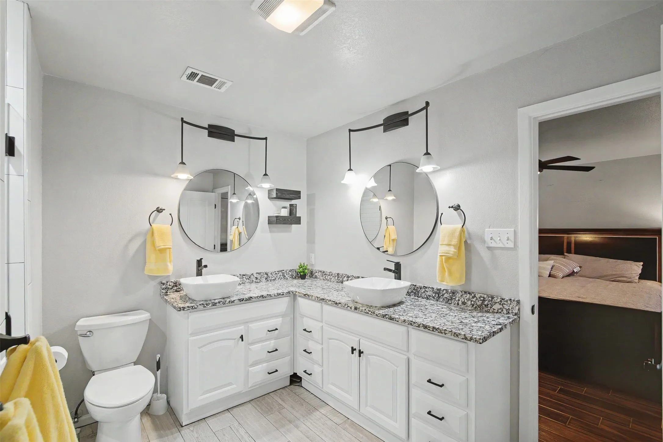 Dual vanity featuring white cabinetry, stone-patterned countertops, two round mirrors, and black-finish hardware
