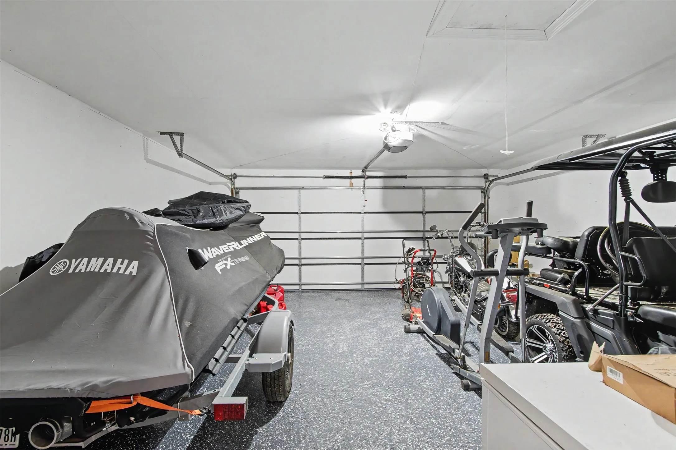Attached garage featuring epoxy flooring, overhead storage access, and automated door opener