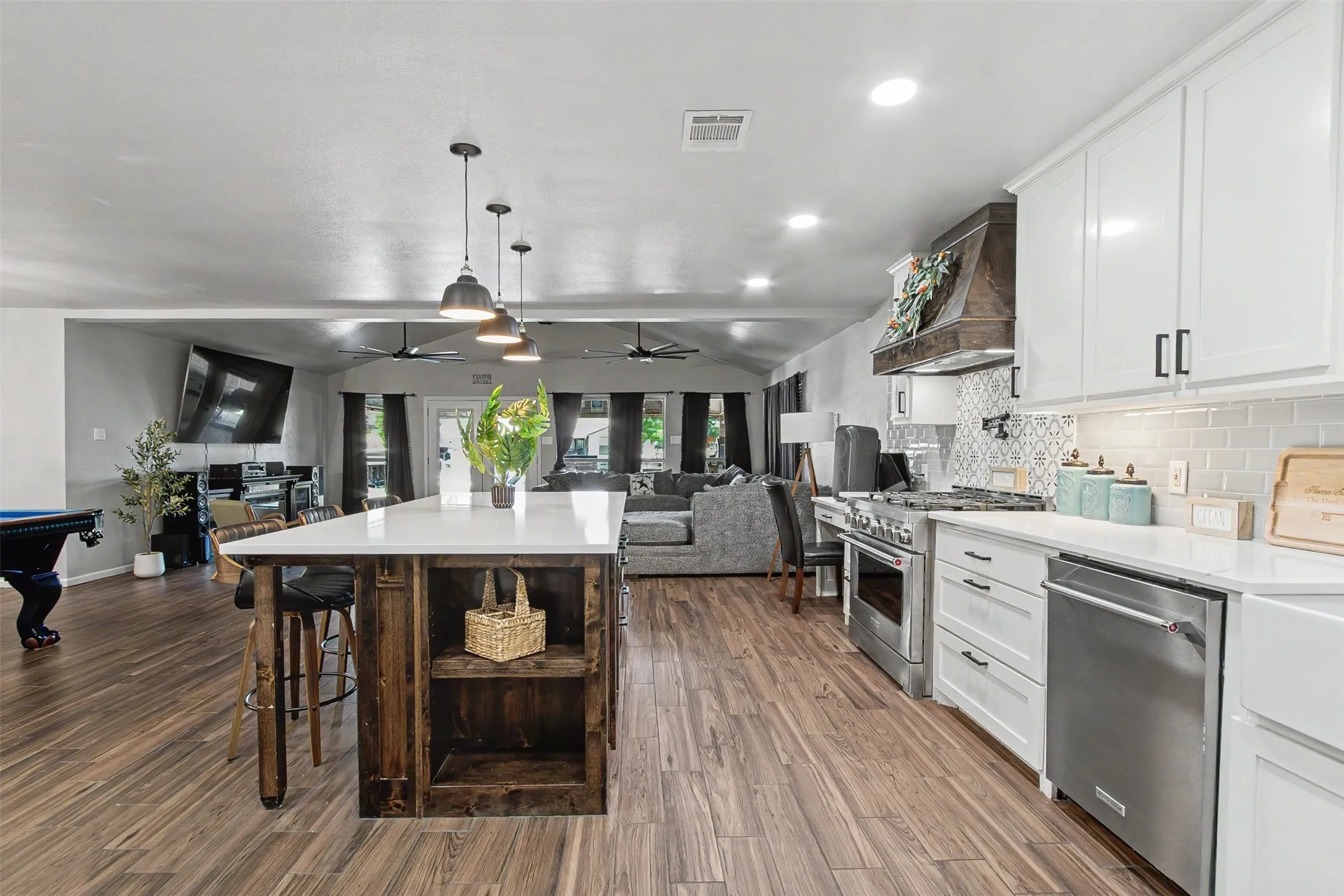 Kitchen featuring a wood-finish island with a white countertop, white cabinetry, stainless steel appliances, a custom wood-encased range hood, and patterned tile backsplash