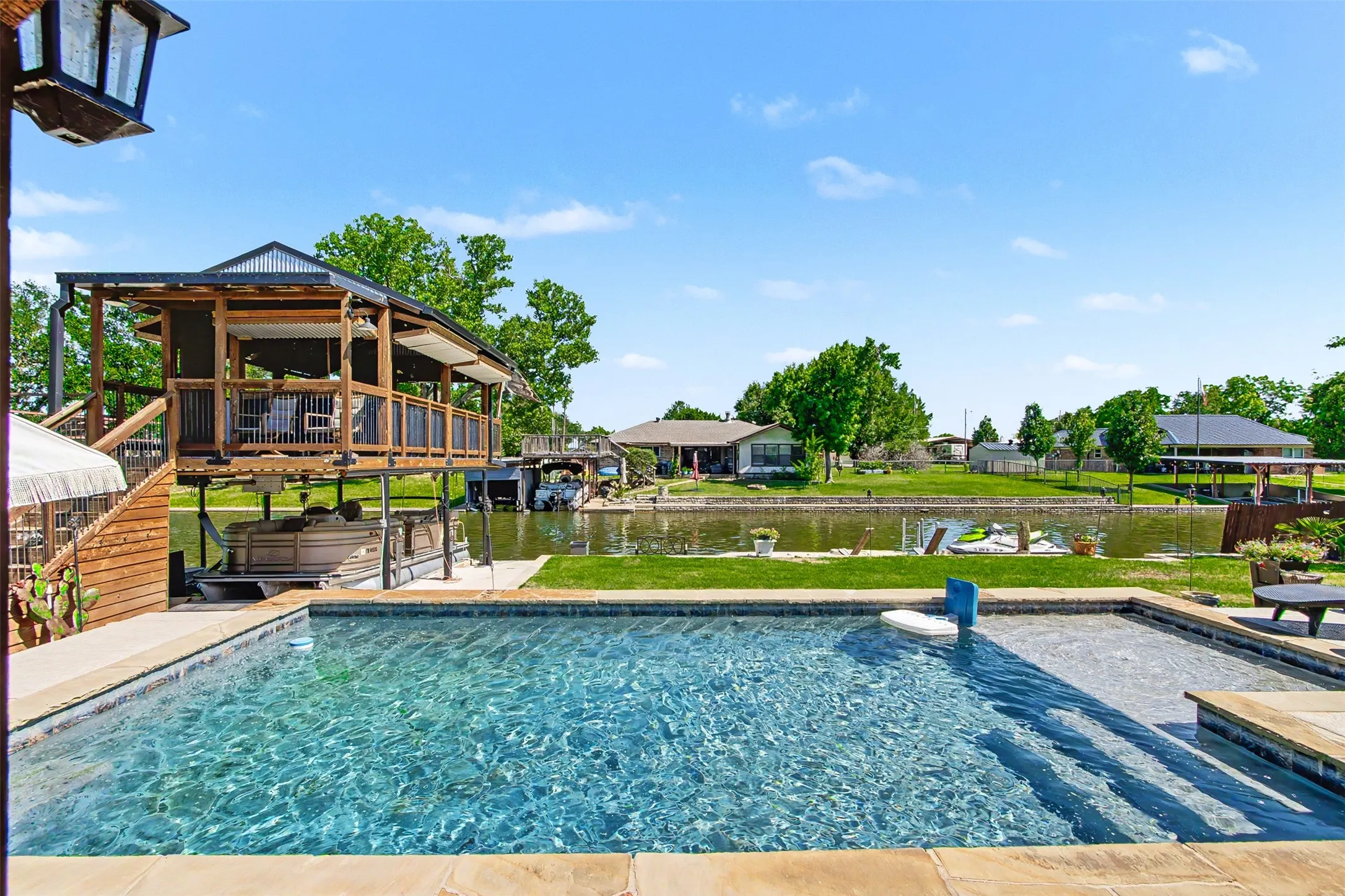 In-ground swimming pool with stone coping, multi-level wooden boat dock with covered slip, and direct water frontage