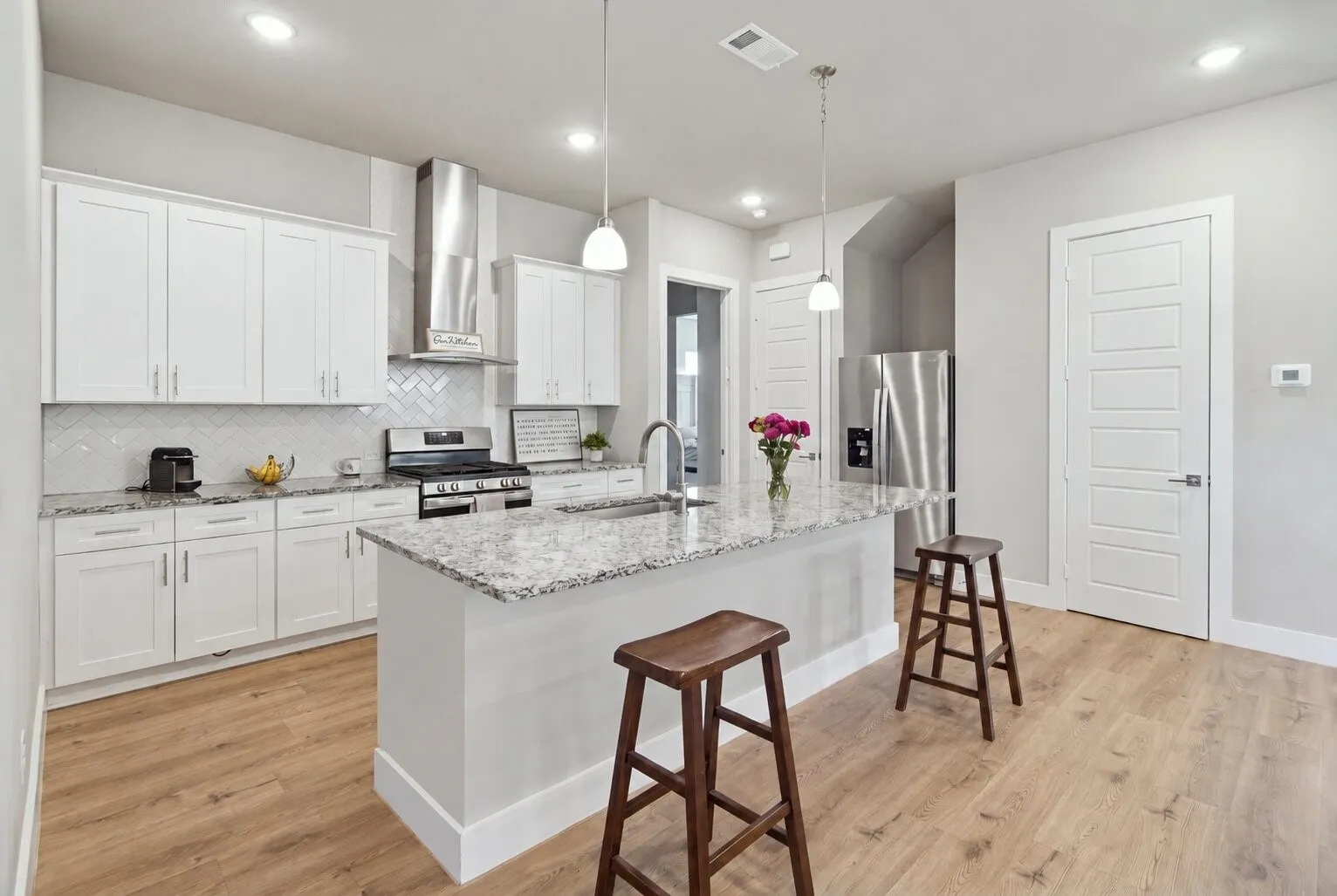Kitchen featuring white cabinetry, stone-surface countertops, chevron-patterned backsplash, stainless steel appliances, and wood-finish flooring