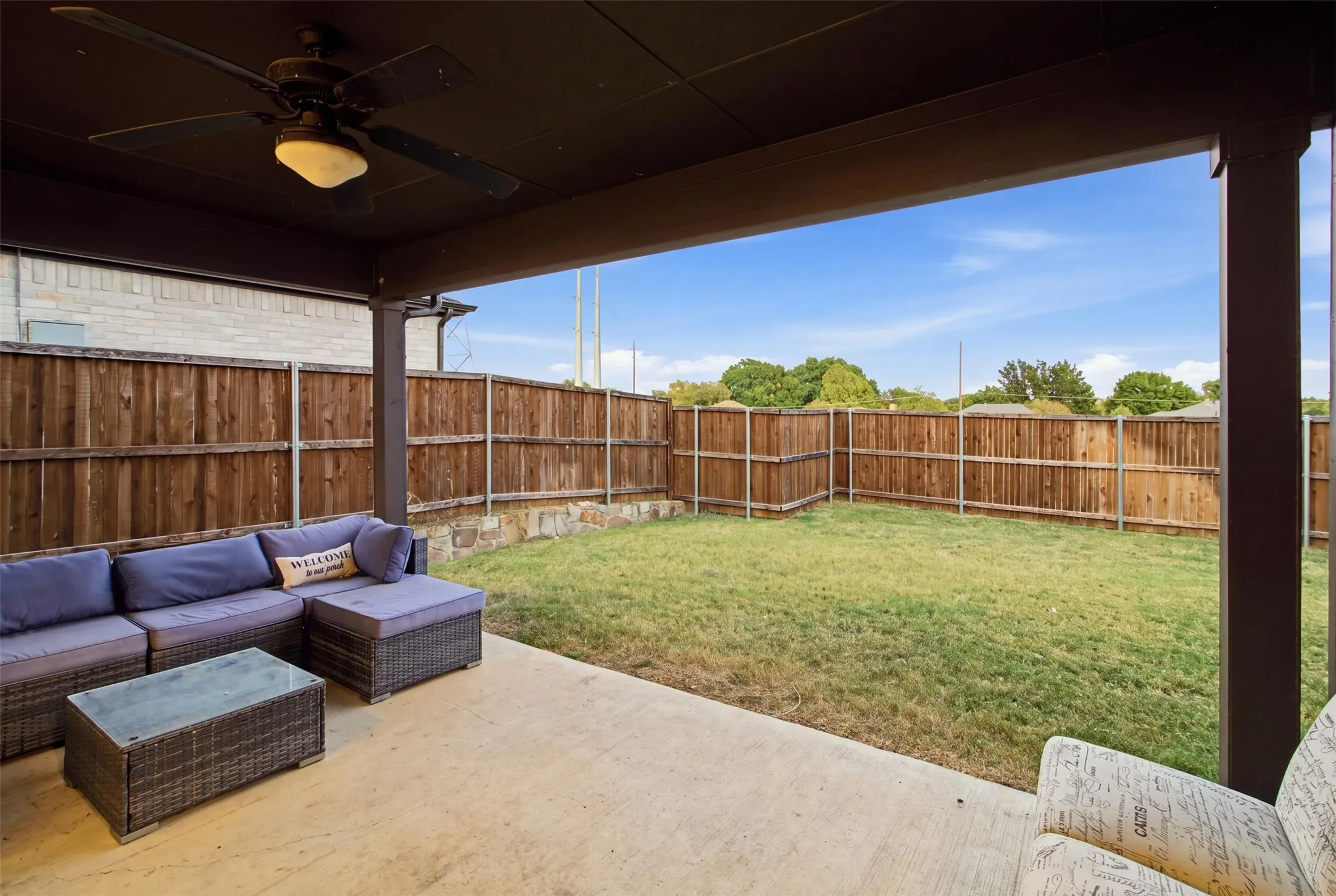 Covered patio featuring a ceiling fan, concrete flooring, stone retaining wall, and wood privacy fencing surrounding the backyard
