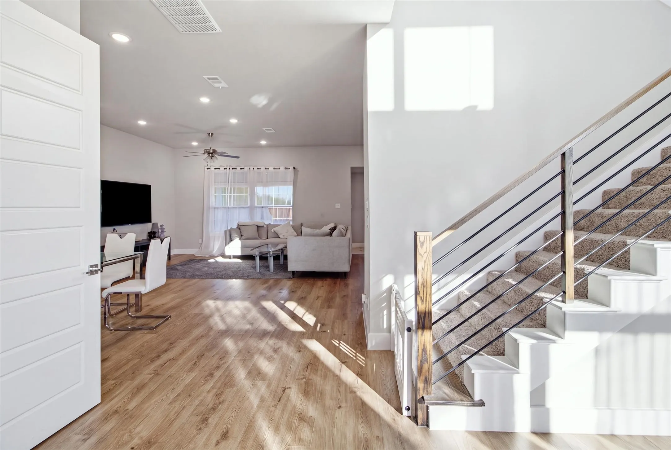 Open-concept interior featuring wood-finish flooring, recessed lighting, and a staircase with a wood handrail and horizontal metal balusters