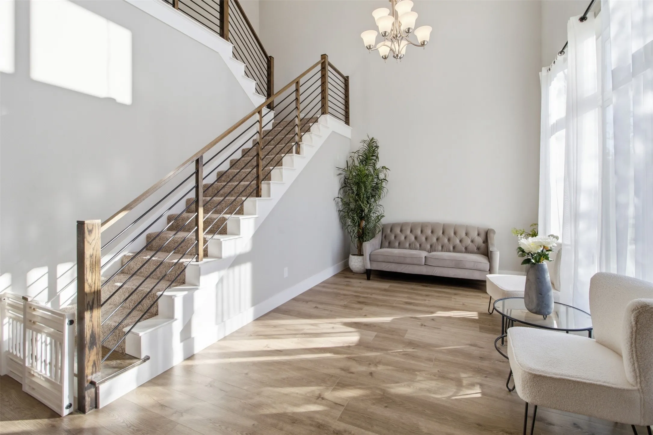 Double-height foyer featuring wood-finish flooring, a grand staircase with horizontal cable railing, and a multi-arm chandelier