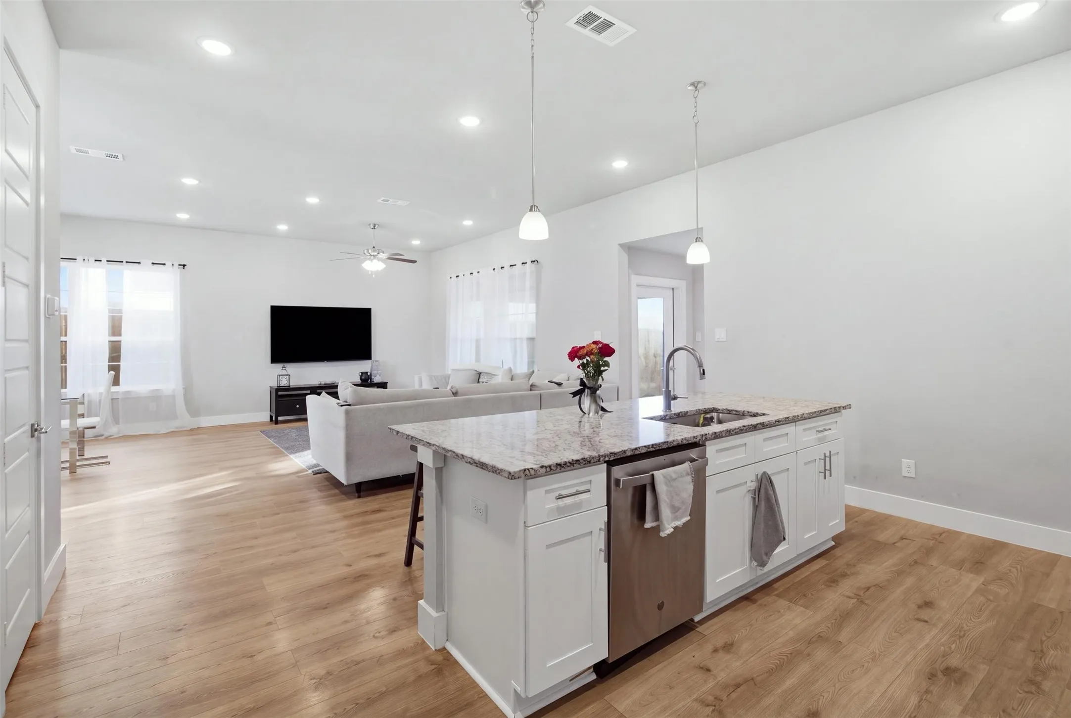Kitchen island with stone-surface countertop, stainless steel dishwasher, white cabinetry, wood-finish flooring, and recessed ceiling lighting