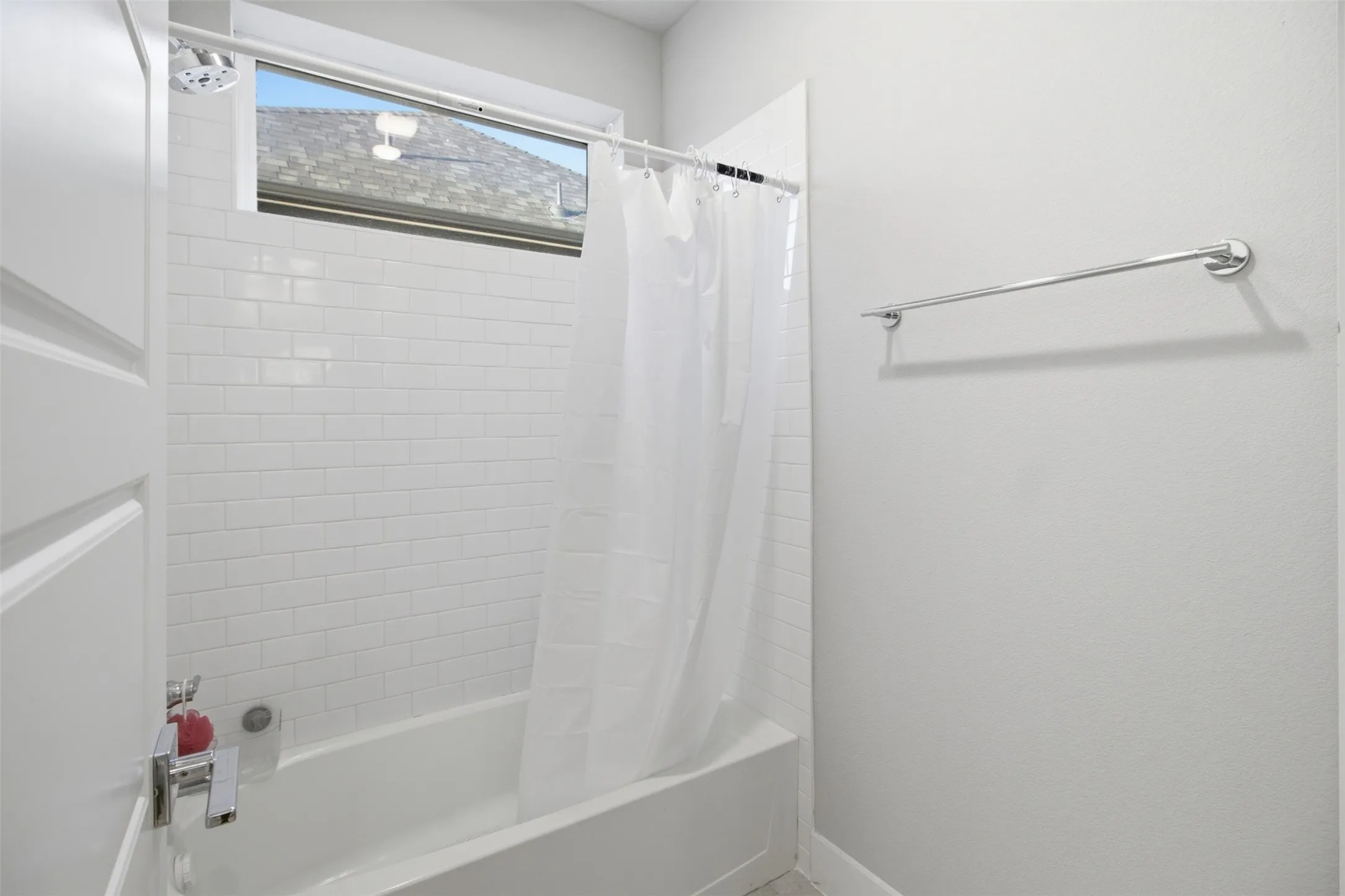 Tub and shower combination featuring white subway tile surround, high-set horizontal window, and polished chrome hardware