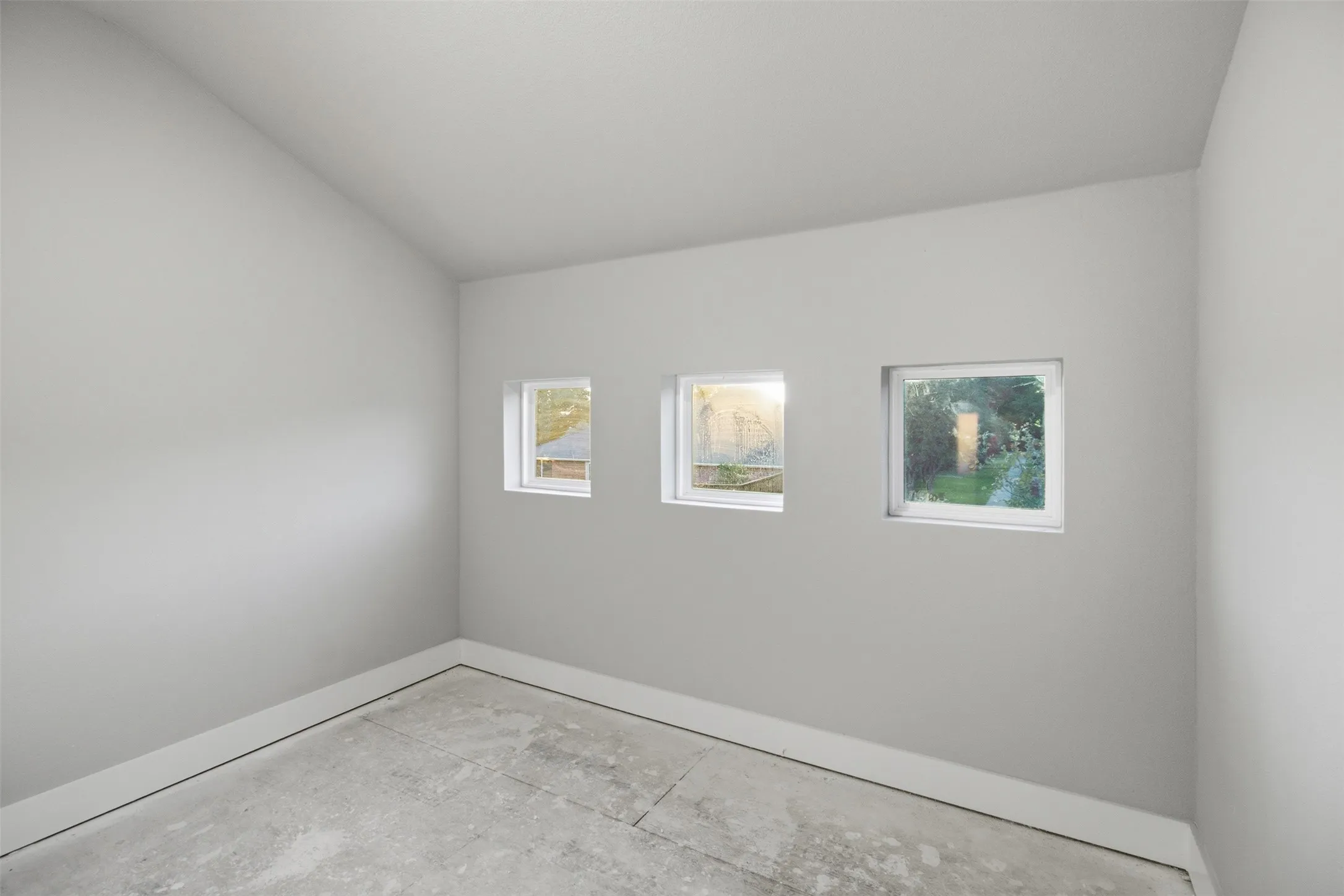 Vaulted ceiling room featuring three inset square windows and concrete flooring