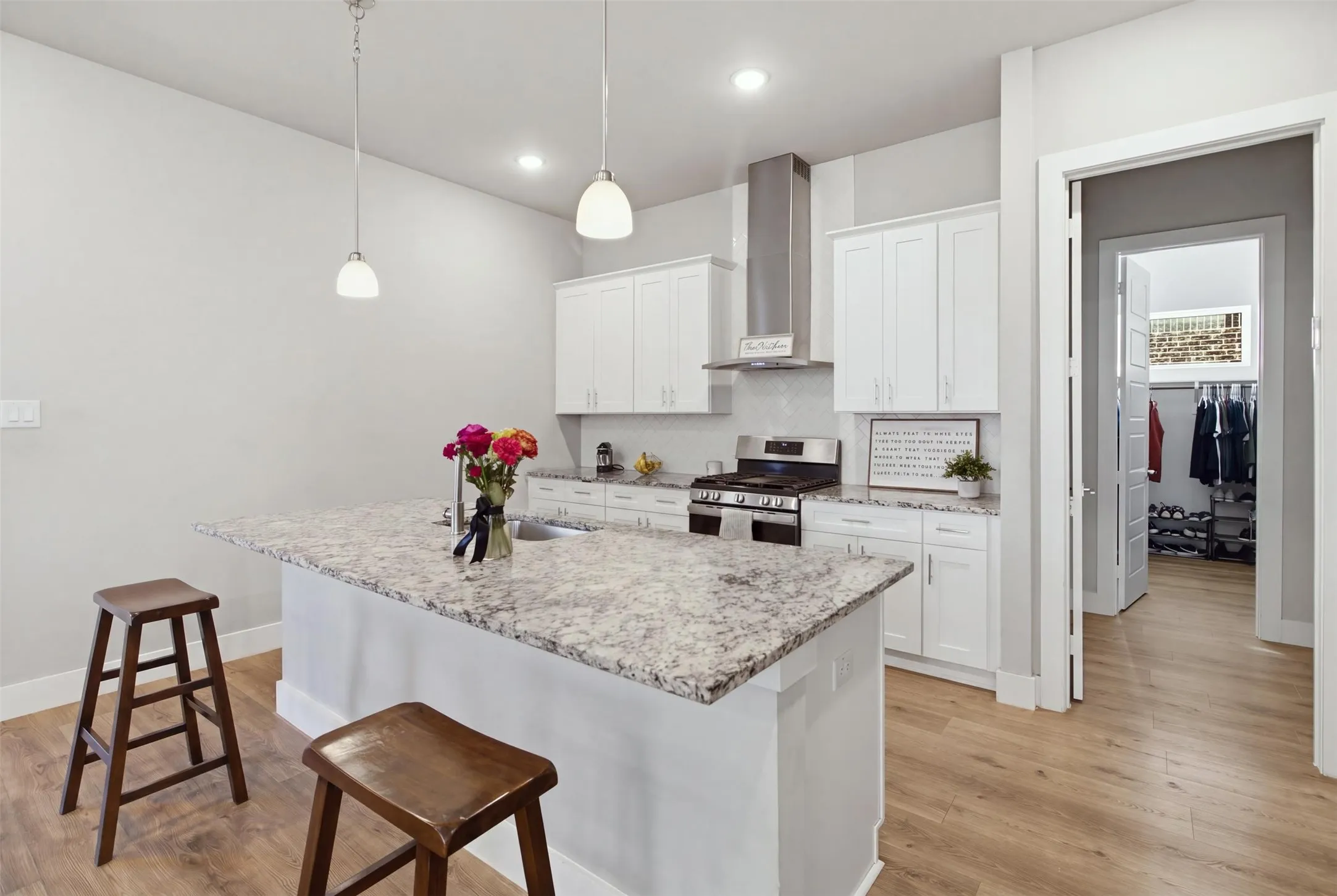 Kitchen featuring white cabinetry, stone countertops, stainless steel range with chimney-style hood, pendant lighting, and wood-finish flooring