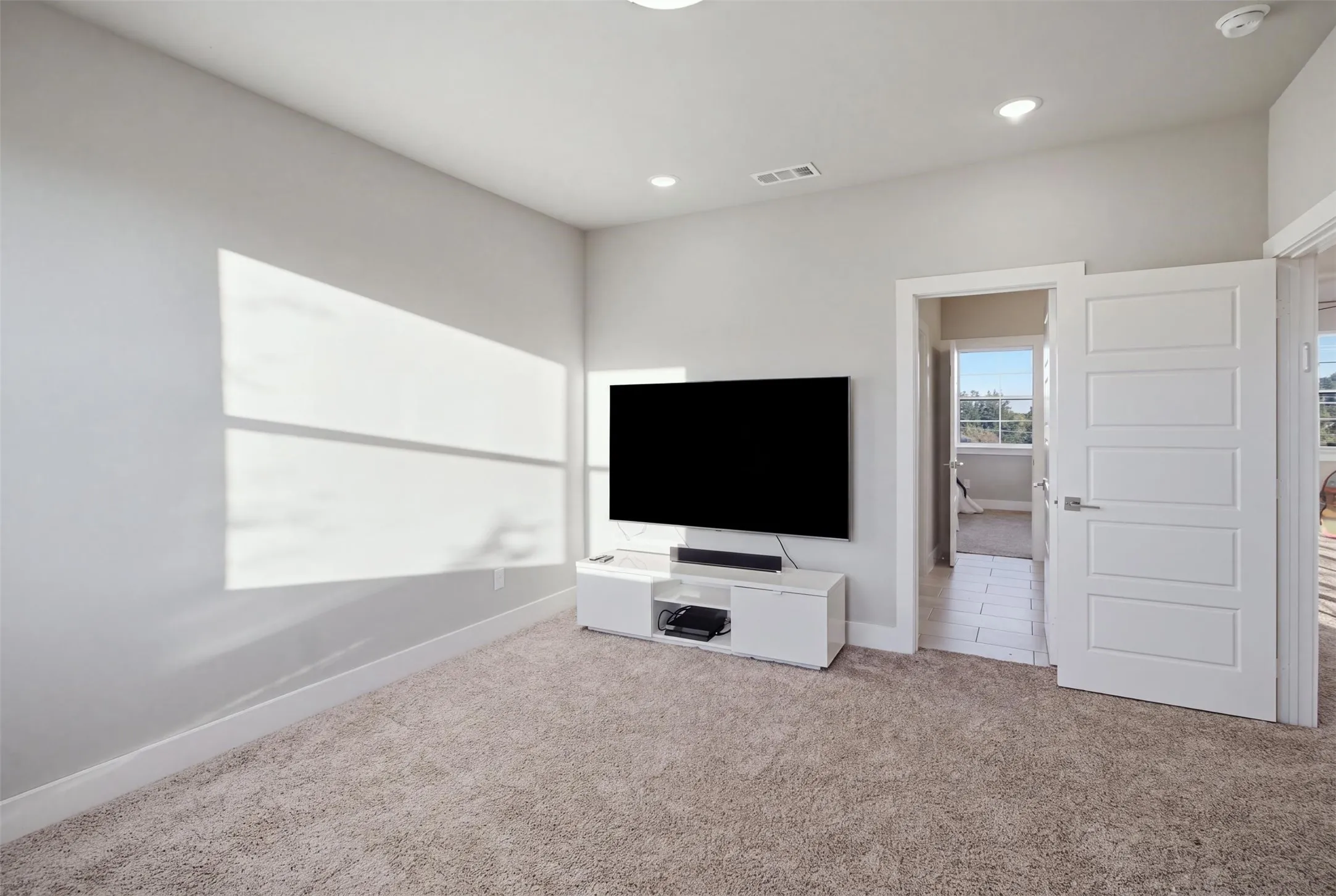 Neutral-toned interior space featuring recessed ceiling lighting, wall-to-wall carpeting, and a four-panel interior door